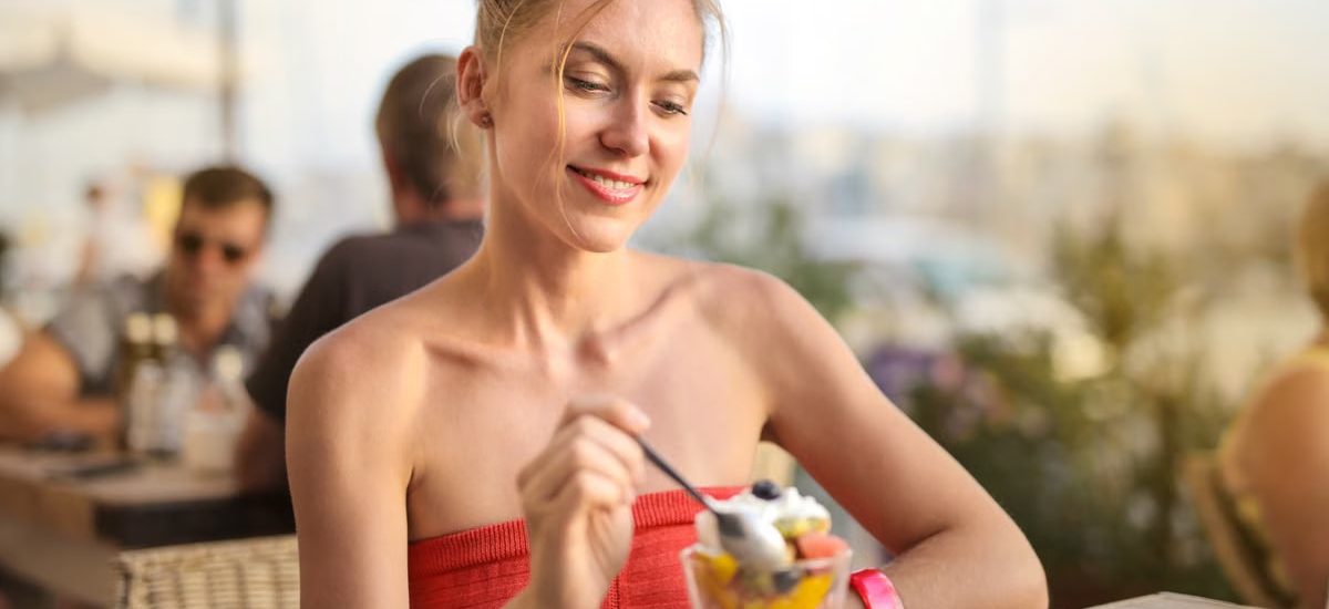 Smiling woman relishes a delicious dessert in a relaxed outdoor cafe setting.