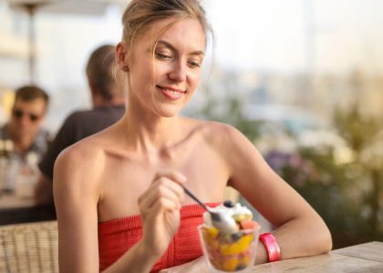 Smiling woman relishes a delicious dessert in a relaxed outdoor cafe setting.